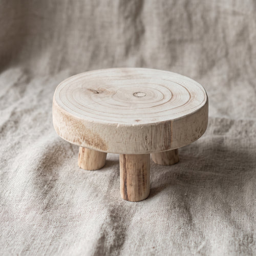 Round pale wooden tray table on oatmeal linen, 45-degree view showing natural grain