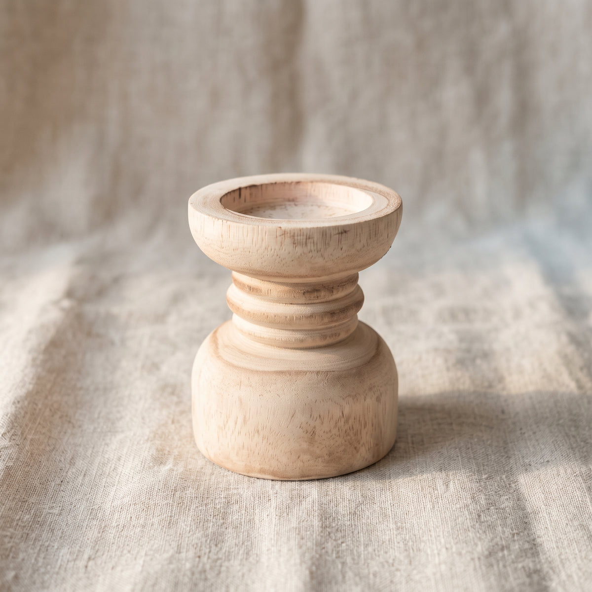 Turned wooden candle holder on light natural linen, 45-degree view